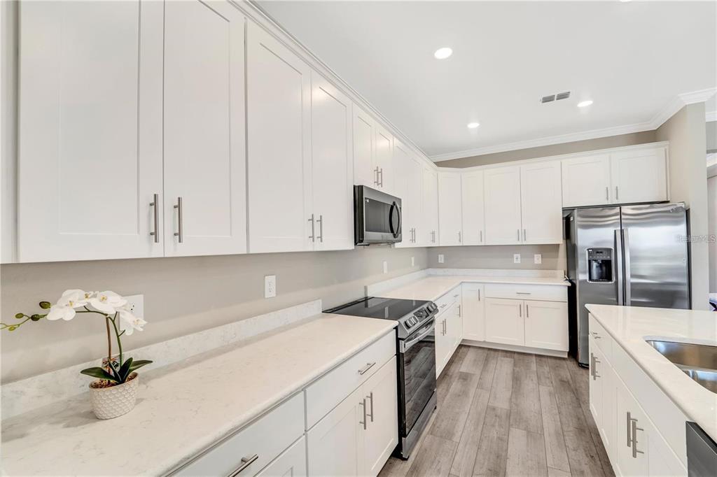A modern kitchen features white cabinetry, stainless steel appliances, and light-colored quartz countertops — 16807 CAYO KEY DRIVE, PORT CHARLOTTE, FL