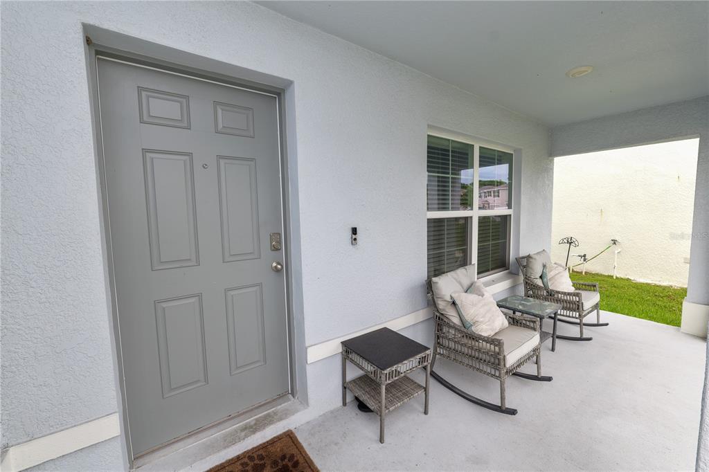 A covered front porch features a gray door, two rocking chairs, and a small table — 3715 CAPRI COAST DRIVE, PLANT CITY, FL
