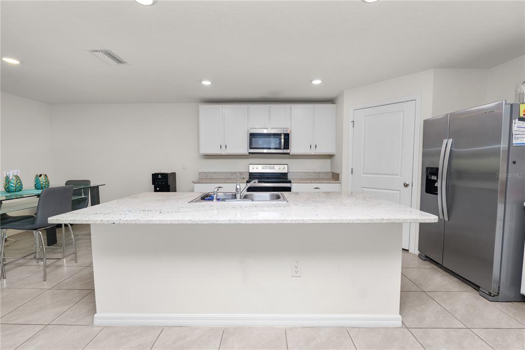 A kitchen features a large granite-topped island, white cabinetry, and stainless steel appliances — 3715 CAPRI COAST DRIVE, PLANT CITY, FL