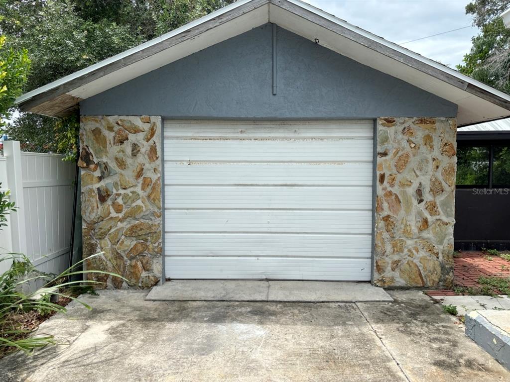 A detached garage features a white roll-up door flanked by stone veneer walls — 1169 KINGSLEY STREET, CLEARWATER, FL
