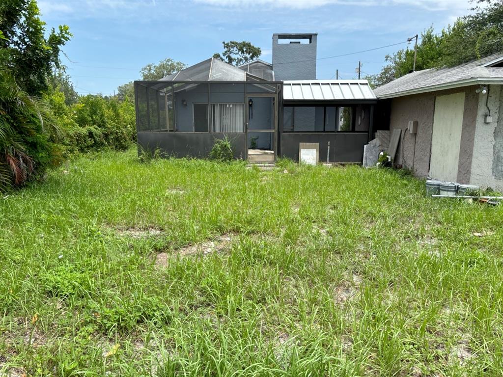 The backyard features a screened-in porch, a metal-roofed addition, and an overgrown grassy lawn — 1169 KINGSLEY STREET, CLEARWATER, FL