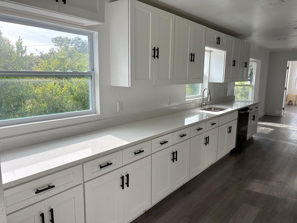 A kitchen features white shaker cabinets, quartz countertops, black hardware, and a stainless steel sink — 1169 KINGSLEY STREET, CLEARWATER, FL