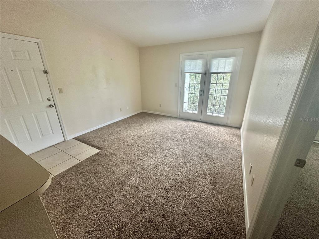 An empty room features beige carpet, a white entry door, and glass French doors — 2550 N ALAFAYA TRAIL UNIT 10305, ORLANDO, FL