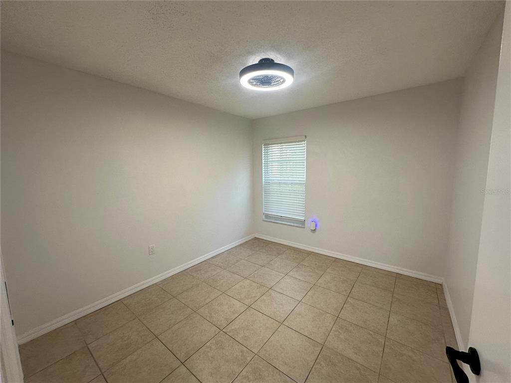 An empty bedroom features light-colored walls, a tiled floor, and a ceiling fan light fixture — 2838 OSPREY COVE PLACE UNIT 103, KISSIMMEE, FL