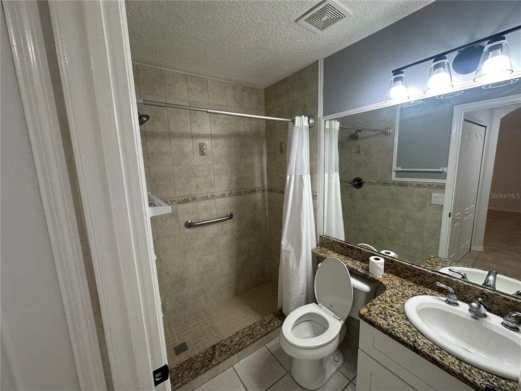 A bathroom features a tiled walk-in shower, a toilet, and a granite-topped vanity — 2838 OSPREY COVE PLACE UNIT 103, KISSIMMEE, FL