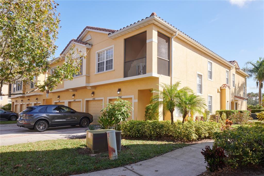 A multi-story tan townhouse with a screened balcony, attached garages, and a parked SUV — 2745 OAKWATER DRIVE, KISSIMMEE, FL