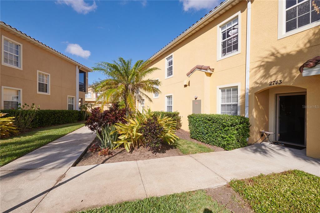 A two-story yellow stucco apartment building features a palm tree and a paved walkway — 2745 OAKWATER DRIVE, KISSIMMEE, FL