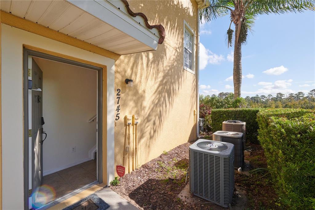 An exterior view of a building entrance with three air conditioning units and landscaping — 2745 OAKWATER DRIVE, KISSIMMEE, FL