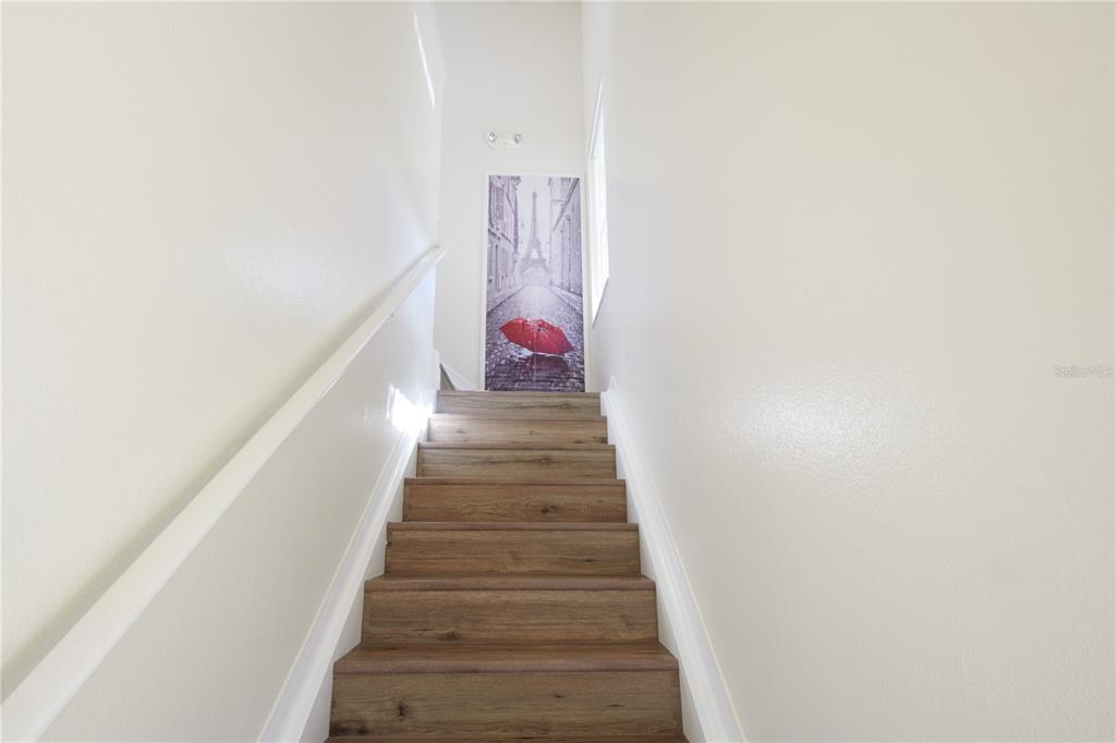 A staircase with wood-look steps leads to a landing featuring a tall Paris-themed wall art piece — 2745 OAKWATER DRIVE, KISSIMMEE, FL