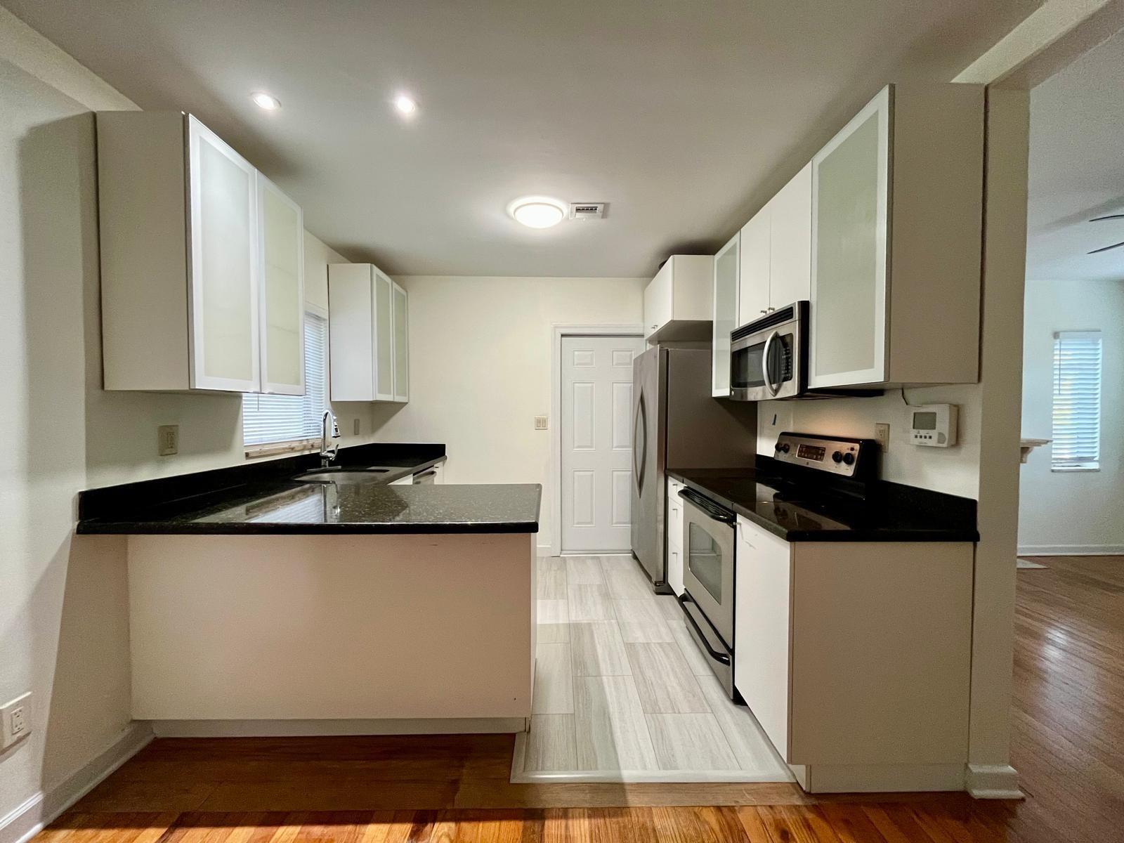 A kitchen with white cabinets, black countertops, stainless steel appliances, and light-colored tile flooring — 348 Gregory Road, West Palm Beach FL 33405, WEST PALM BEACH, FL