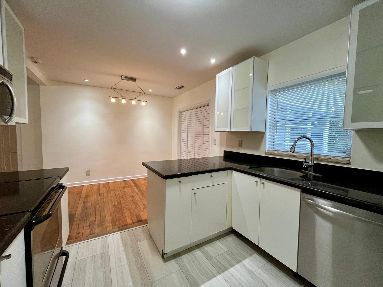 A kitchen with white cabinets, black countertops, and a dining area with hardwood floors — 348 Gregory Road, West Palm Beach FL 33405, WEST PALM BEACH, FL