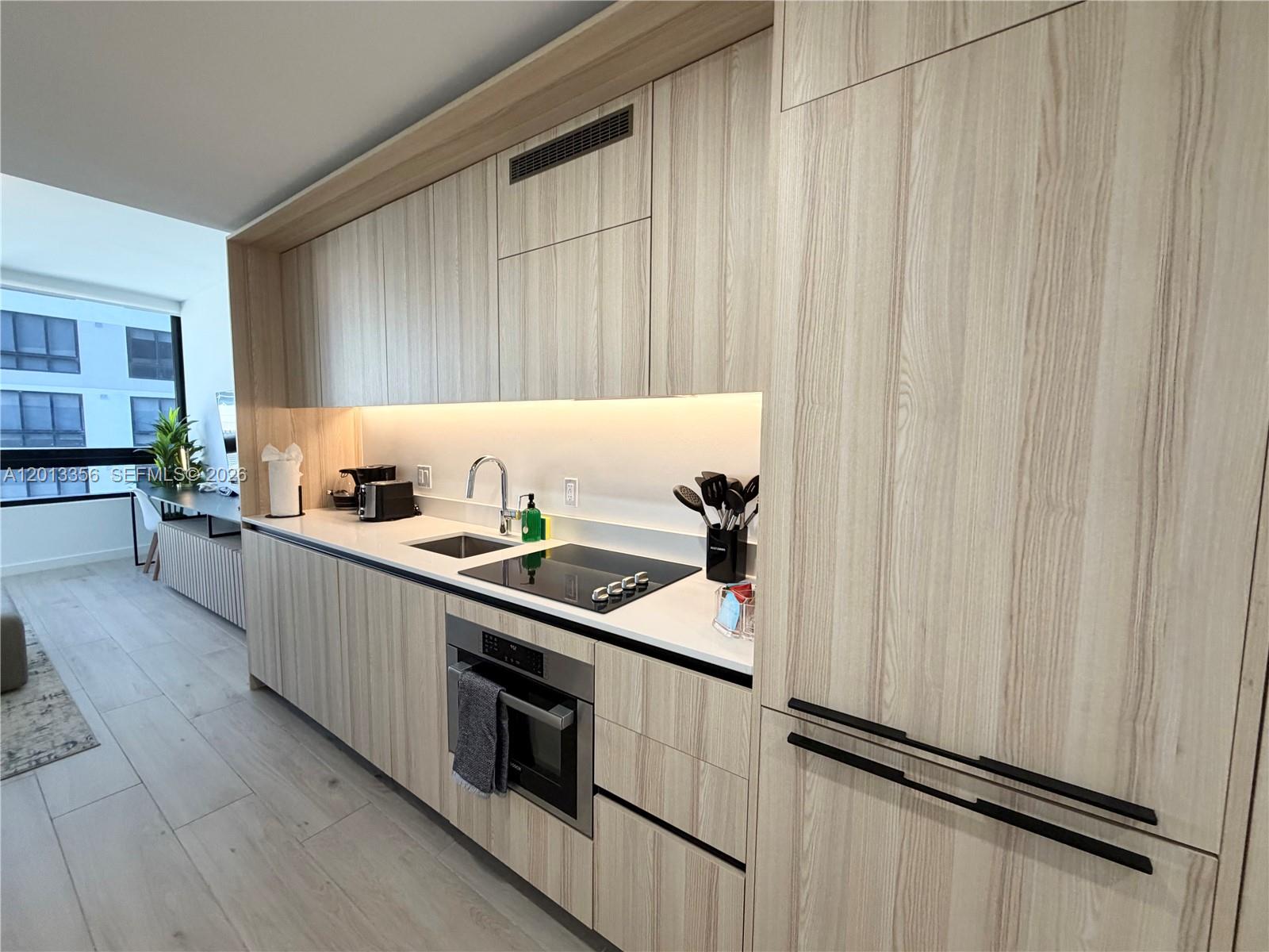 A modern kitchen features light wood-grain cabinetry, integrated appliances, and a white countertop — 225 N Miami Ave # 1412, Miami FL 33128, MIAMI, FL
