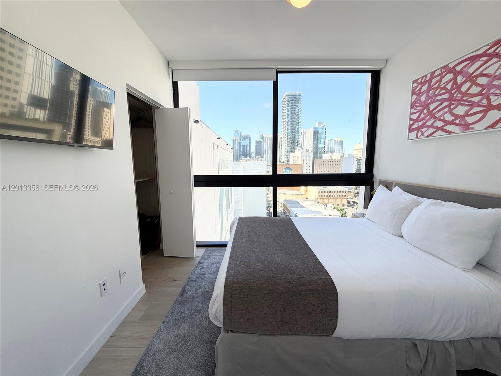 A bedroom features a bed, a wall-mounted television, a closet, and floor-to-ceiling city views — 225 N Miami Ave # 1412, Miami FL 33128, MIAMI, FL
