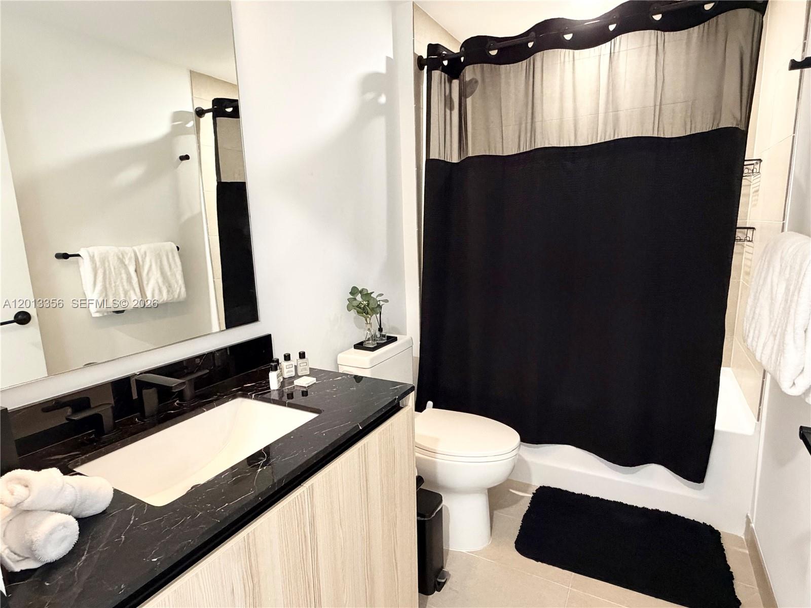 A bathroom features a black marble vanity, light wood cabinetry, and a black shower curtain — 225 N Miami Ave # 1412, Miami FL 33128, MIAMI, FL