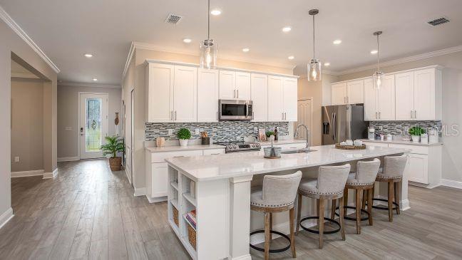 A modern kitchen features white cabinetry, a large quartz island with seating, and wood-look flooring — TBD KNOTTY PINE AVENUE, NORTH PORT, FL