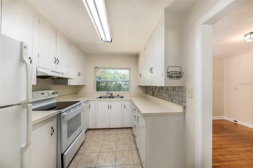 A galley kitchen features white cabinets, white appliances, tiled flooring, and a window above the sink — 519 VERN DRIVE, ORLANDO, FL