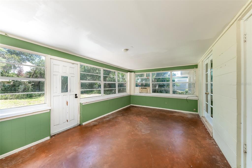 A sunroom with green paneled walls, a concrete floor, and multiple windows — 519 VERN DRIVE, ORLANDO, FL