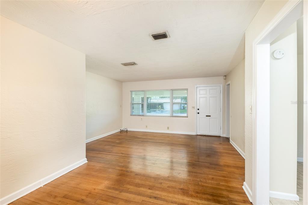 An empty room with hardwood floors, a white front door, and a large window — 519 VERN DRIVE, ORLANDO, FL