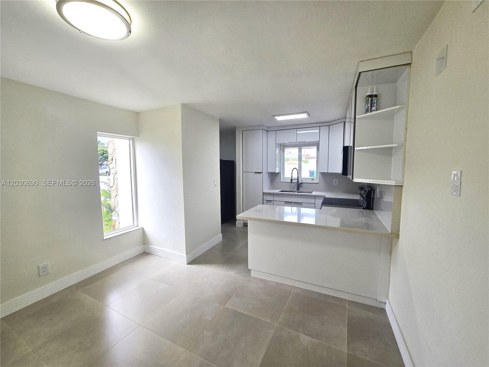 A modern kitchen features white cabinetry, a peninsula, and light tile flooring — 8891 SW 36th St # 8891, Miami FL 33165, MIAMI, FL
