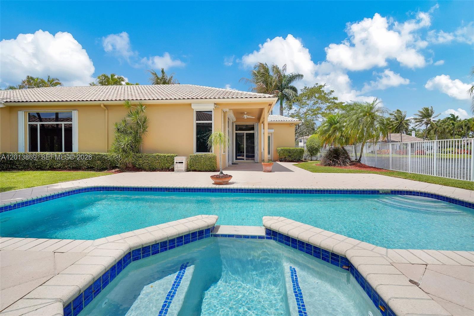 A backyard features a swimming pool and spa with a patio and a yellow house — 2456 Bay Isle Court, Weston FL 33327, WESTON, FL