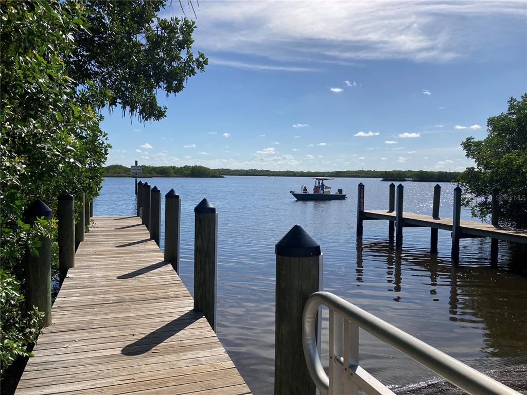 A wooden dock extends into a calm bay with a boat visible in the distance — 25187 PALISADE ROAD, PUNTA GORDA, FL
