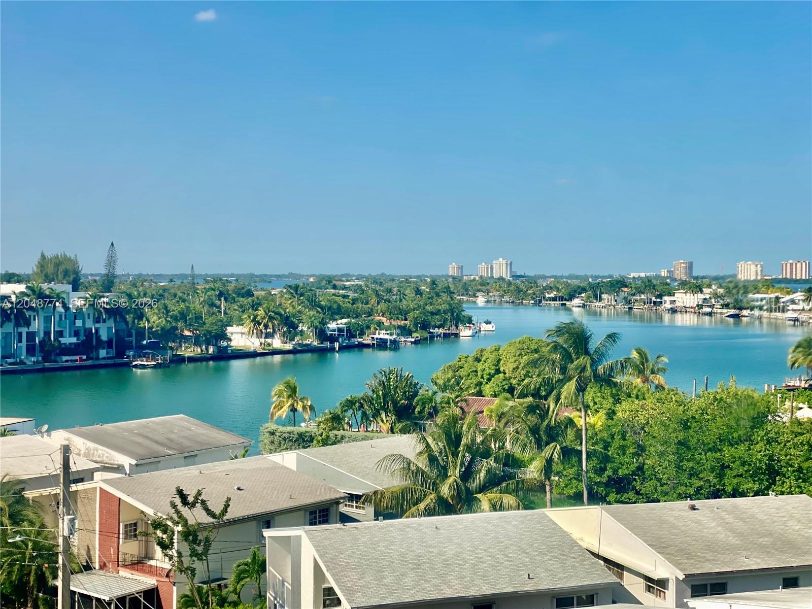An elevated view shows a canal surrounded by lush trees, residential rooftops, and distant buildings — 7441 Wayne Ave # 6B, Miami Beach FL 33141, MIAMI BEACH, FL