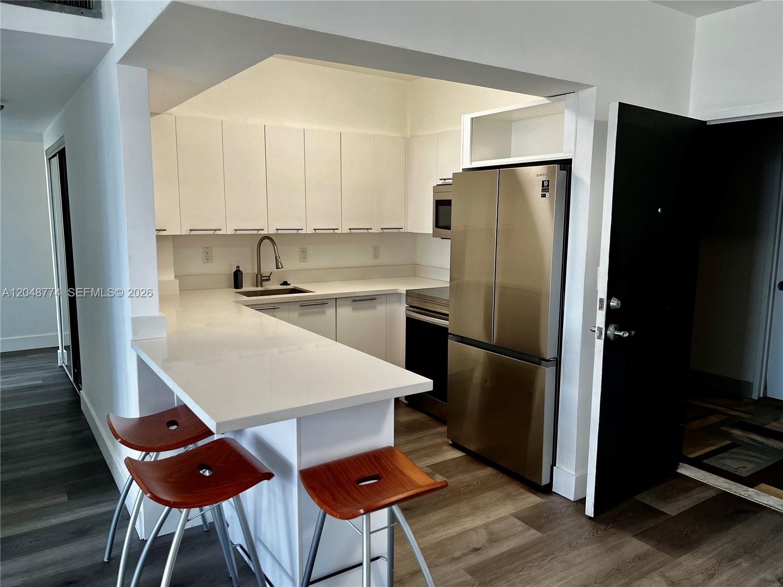 A modern kitchen features white cabinets, stainless steel appliances, and a breakfast bar with stools — 7441 Wayne Ave # 6B, Miami Beach FL 33141, MIAMI BEACH, FL