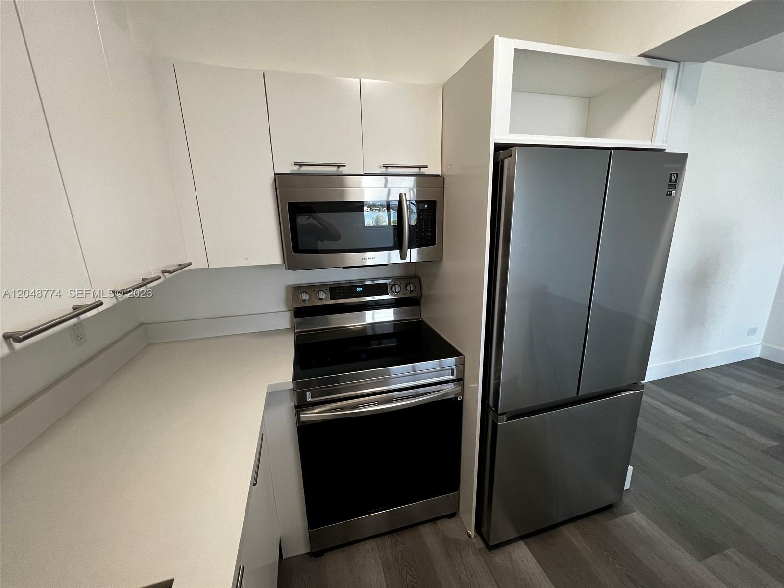 A kitchen features white cabinets, stainless steel appliances, and gray wood-look flooring — 7441 Wayne Ave # 6B, Miami Beach FL 33141, MIAMI BEACH, FL