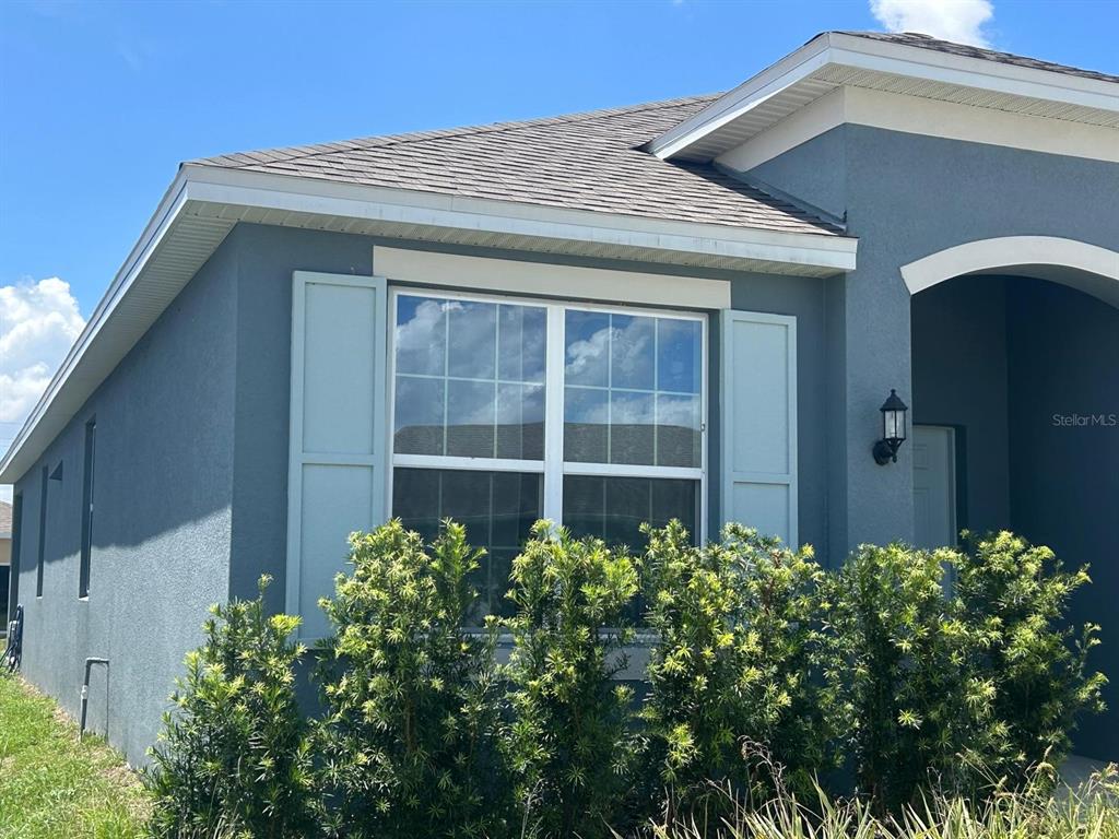 The exterior of a blue stucco house features a window with shutters and landscaping — 468 SILVER PALM DRIVE, HAINES CITY, FL