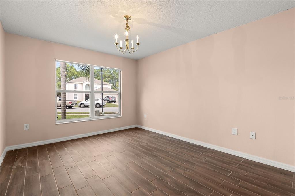 An empty room features light pink walls, wood-look tile flooring, and a central chandelier — 4232 STONEFIELD DRIVE, ORLANDO, FL