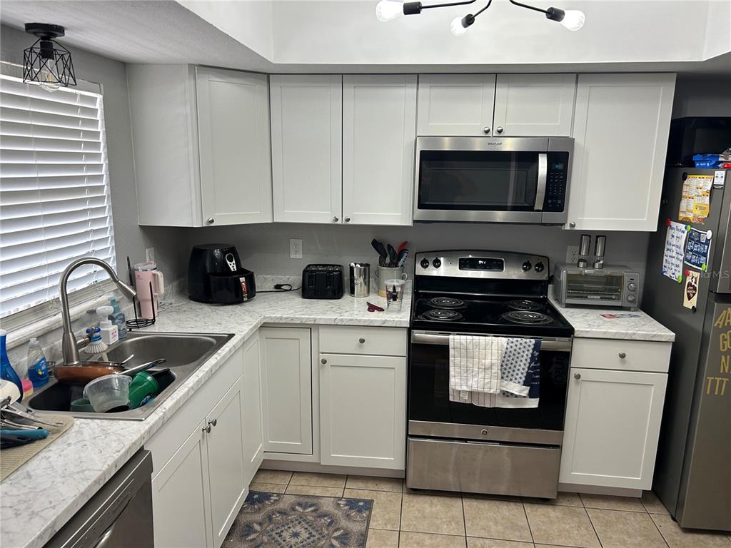 A kitchen features white cabinets, marble-look countertops, stainless steel appliances, and a tile floor — 6301 58TH STREET N UNIT 602, PINELLAS PARK, FL