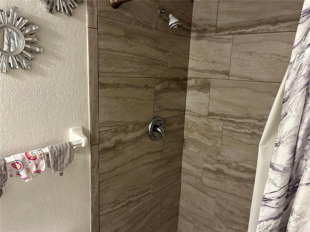 A shower with beige stone-look tile walls, a chrome faucet, and a showerhead — 6301 58TH STREET N UNIT 602, PINELLAS PARK, FL