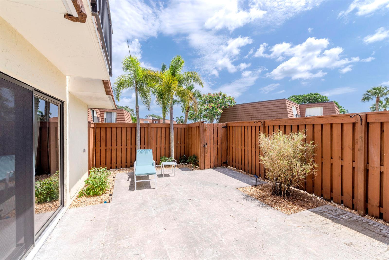 A concrete patio features a lounge chair, small table, and privacy fence under palm trees — 3900 County Line Road # 21a, Tequesta FL 33469, TEQUESTA, FL