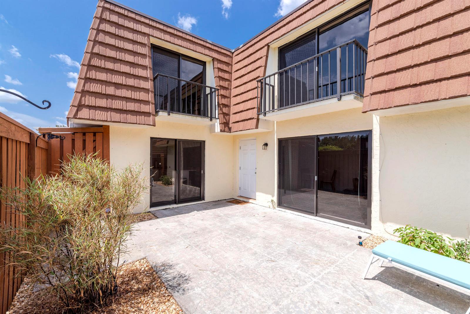 A two-story townhouse exterior features a paved patio, sliding glass doors, and a balcony — 3900 County Line Road # 21a, Tequesta FL 33469, TEQUESTA, FL