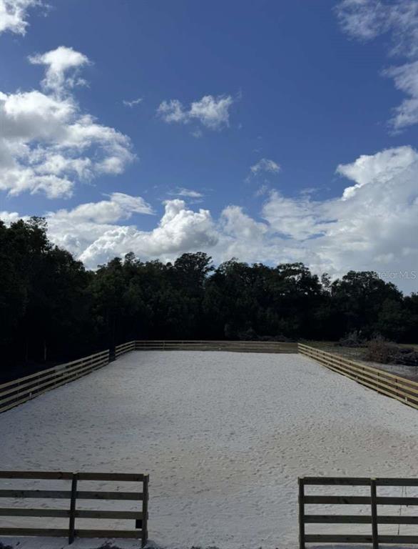A fenced, rectangular sand riding arena is surrounded by trees under a blue sky — 4260 NW 96TH LANE, OCALA, FL