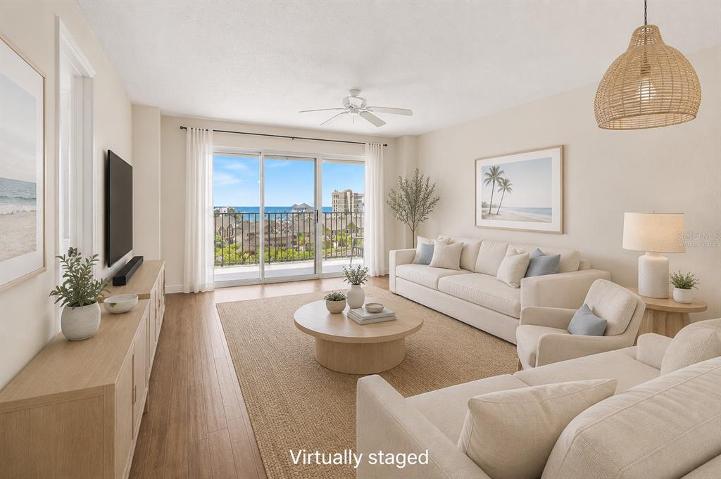 This virtually staged living room features light wood flooring, a balcony, and ocean views — 4 OCEANS WEST BLVD UNIT 606D, DAYTONA BEACH SHORES, FL