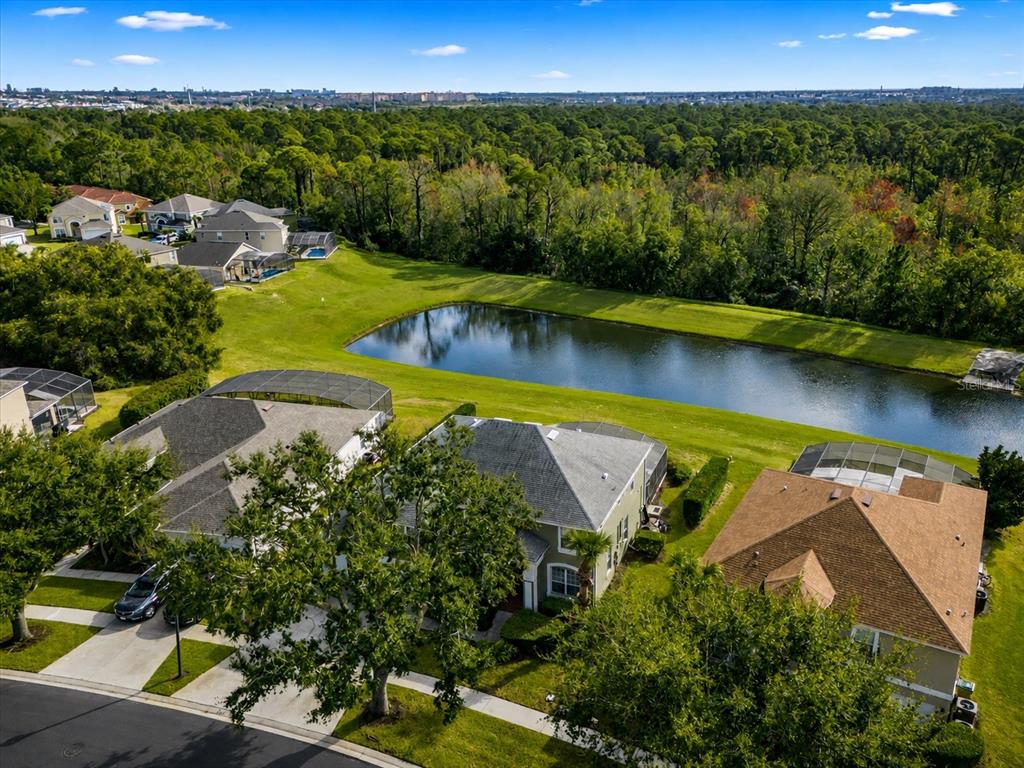 An aerial view of suburban houses with screened-in pools overlooking a pond and wooded area — 8511 LA ISLA DRIVE, KISSIMMEE, FL
