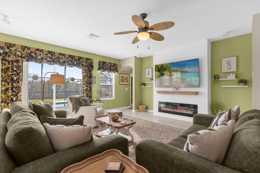 A living room features green walls, a fireplace with a mounted television, and a ceiling fan — 8511 LA ISLA DRIVE, KISSIMMEE, FL