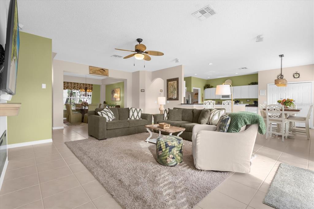 An open-concept living room features a beige rug, olive green sofas, and a dining area — 8511 LA ISLA DRIVE, KISSIMMEE, FL