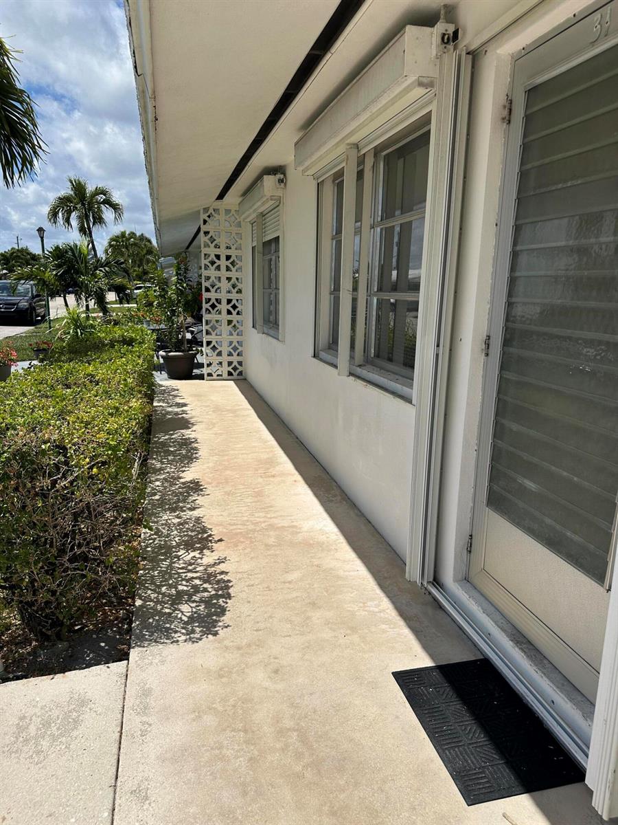 A concrete walkway runs along the side of a white building with windows and shutters — 728 Ridge Road # 31, Lantana FL 33462, LANTANA, FL