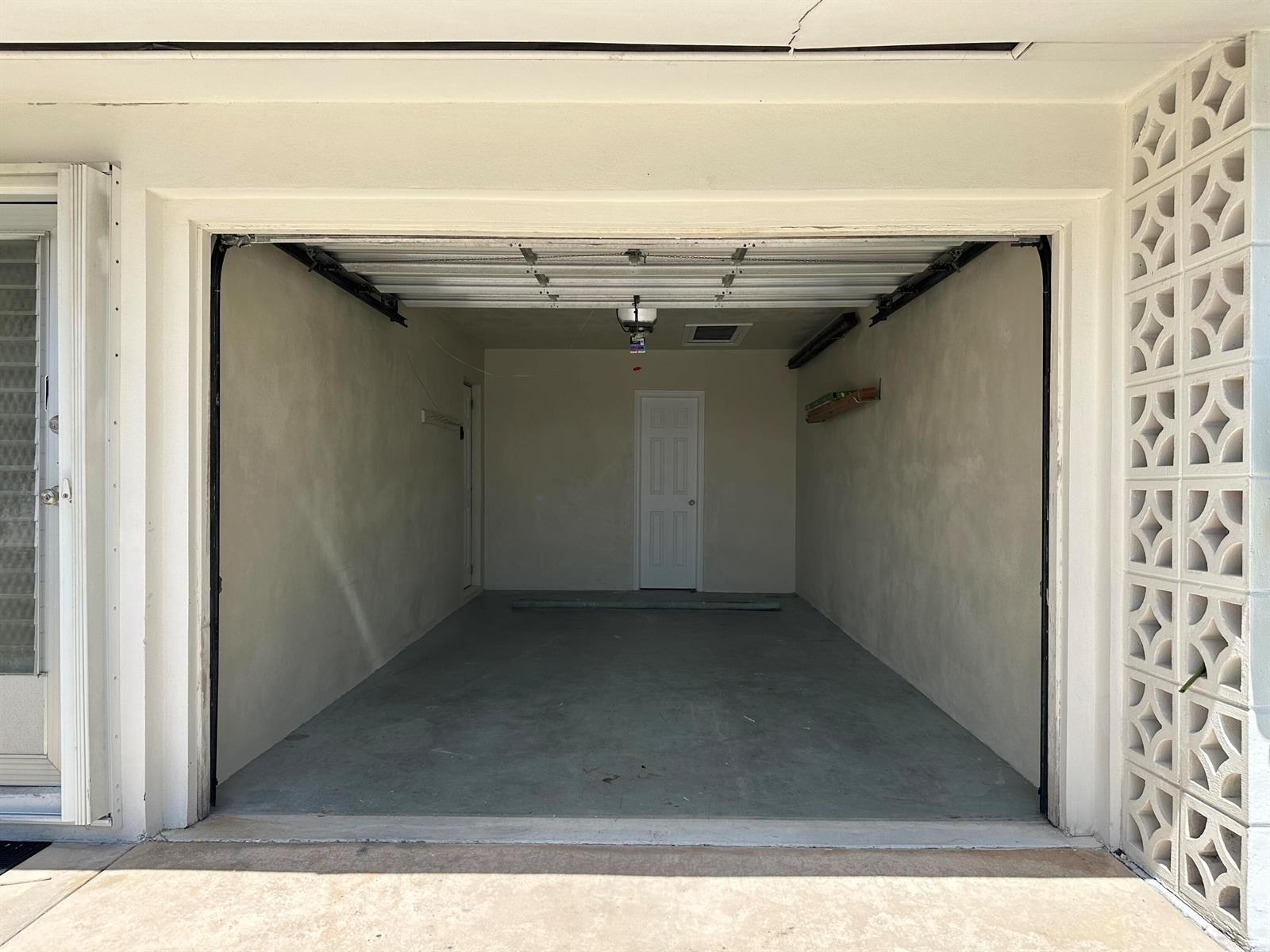 An empty one-car garage with concrete floors, beige walls, and a white interior door — 728 Ridge Road # 31, Lantana FL 33462, LANTANA, FL