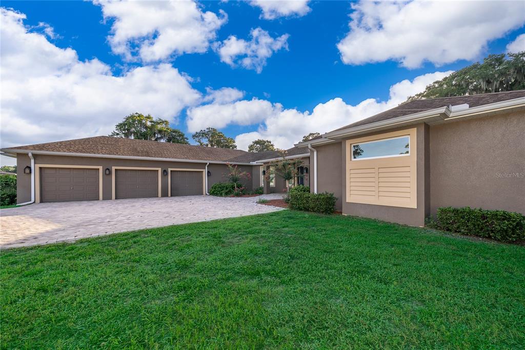 A brown house with a three-car garage and a paved driveway under a cloudy sky — 12131 EAGLES POINT COURT, GRAND ISLAND, FL