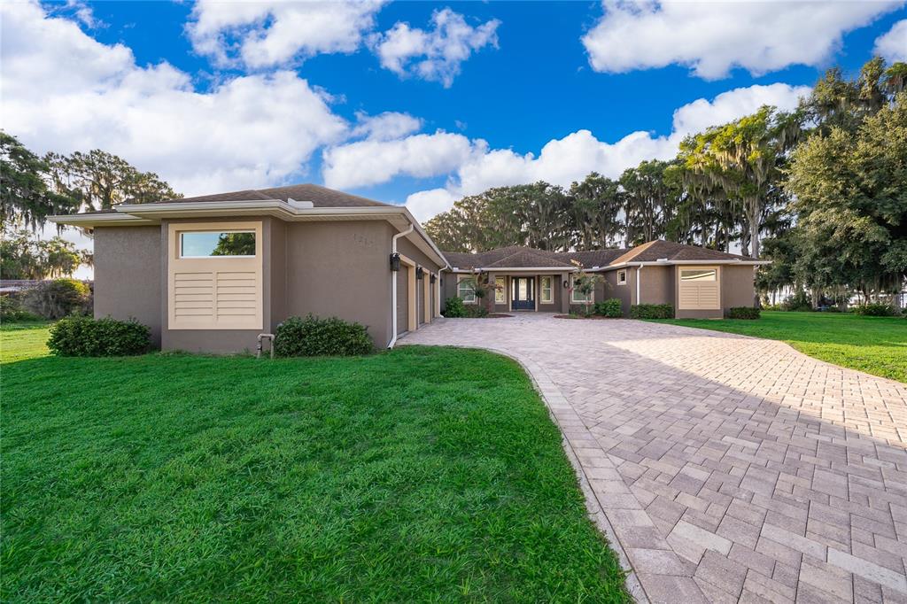 A single-story house with a paved driveway, brown exterior, and surrounding trees under a blue sky — 12131 EAGLES POINT COURT, GRAND ISLAND, FL