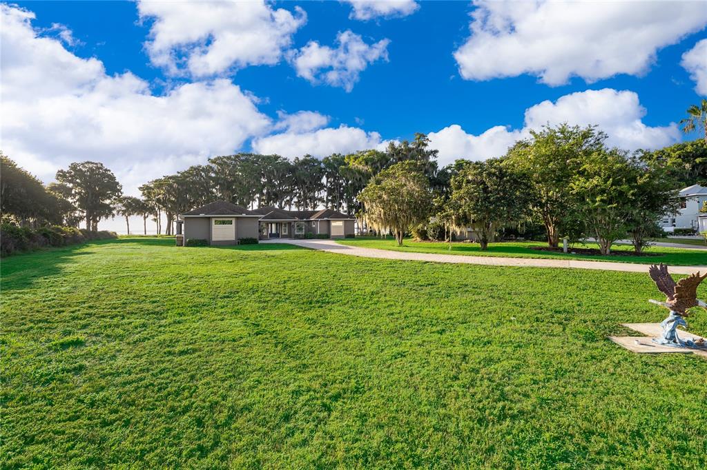 A wide, grassy lawn leads to a single-story house with a paved driveway and trees — 12131 EAGLES POINT COURT, GRAND ISLAND, FL