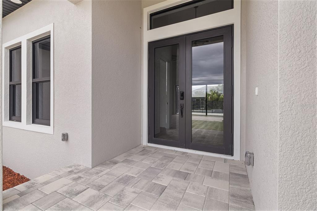 A paved entryway features double glass doors and a window on a light-colored stucco wall — 15381 ALSASK CIRCLE, PORT CHARLOTTE, FL