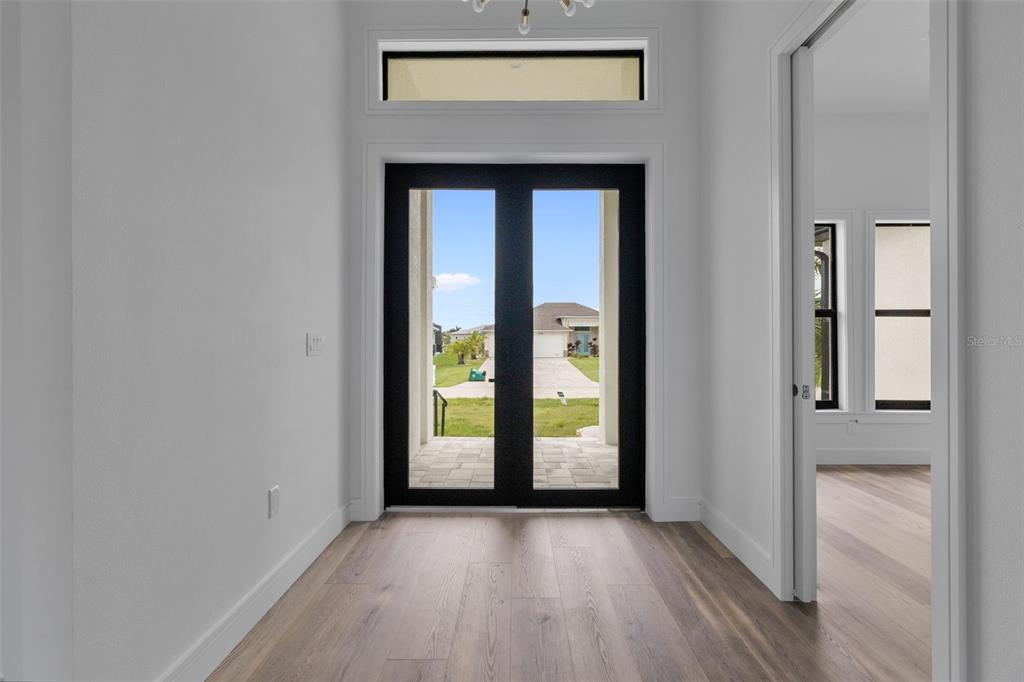 A bright entryway features light wood flooring, white walls, and a black-framed double glass door — 15381 ALSASK CIRCLE, PORT CHARLOTTE, FL