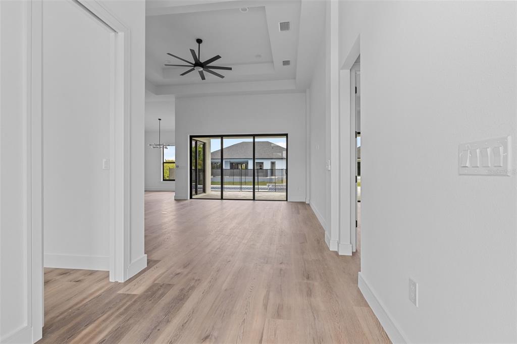 A bright hallway with light wood flooring leads to an open living area with sliding doors — 15381 ALSASK CIRCLE, PORT CHARLOTTE, FL