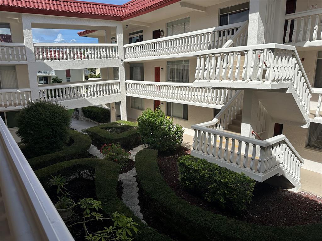 An exterior view of a multi-story apartment complex with white railings and a landscaped courtyard — 2623 SEVILLE BOULEVARD UNIT 202, CLEARWATER, FL
