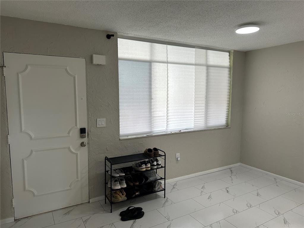 A room with white tile floors, a white door, and a shoe rack under windows — 2623 SEVILLE BOULEVARD UNIT 202, CLEARWATER, FL