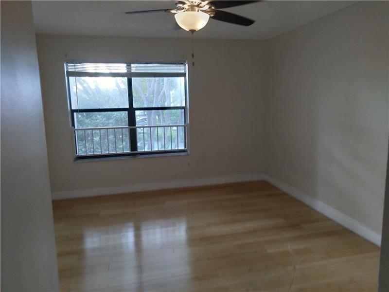 An empty bedroom features light wood flooring, a ceiling fan, and a large window — 4261 W Mcnab Road # 32, Pompano Beach FL 33069, POMPANO BEACH, FL